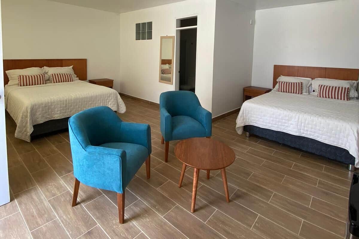 A hotel room with two beds, a sitting area with chairs and a table, and a mirror on the wall.