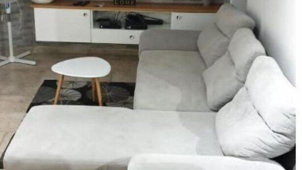 Una sala de estar moderna con un sofá seccional gris, un televisor de pantalla plana montado en una pared con textura similar a la piedra y una pequeña mesita auxiliar blanca.
