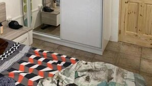 Un dormitorio con cama, armario, espejo y puerta de madera.