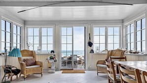 Una habitación amplia con ventanas grandes, mobiliario de mimbre y vistas al mar.