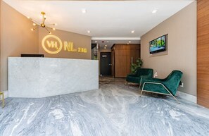 A hotel reception area with a marble floor, a reception desk, and two green chairs.