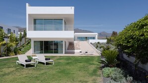 A modern two-story house with a large glass facade, a well-maintained lawn, and outdoor seating. - KARAT Villa Splendida (Playa Paraiso)