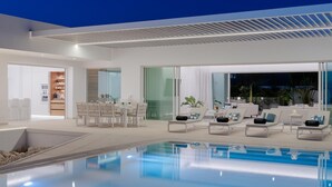 A modern indoor pool area with a dining setup and lounge chairs. - KARAT Villa Splendida (Playa Paraiso)