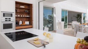 A modern kitchen with a central island, built-in oven, and wooden shelves. - KARAT Villa Splendida (Playa Paraiso)