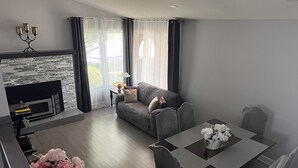 Una sala de estar moderna con chimenea, sofá gris, mesa de comedor y sillas.