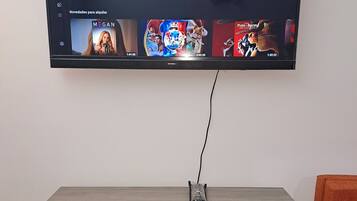 Un televisor de pantalla plana montado en una pared sobre un mueble bajo de madera con un decodificador.