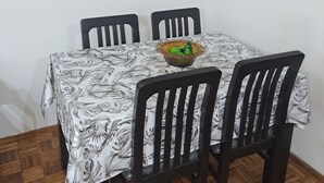 Een eetgedeelte met een tafel bedekt met een bloemrijk tafelkleed, omringd door vier stoelen. Boven de tafel hangen drie ingelijste foto's aan de muur.