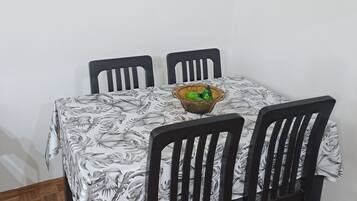 Un comedor con una mesa cubierta por un mantel floral, rodeada por cuatro sillas. Hay tres cuadros en la pared sobre la mesa.