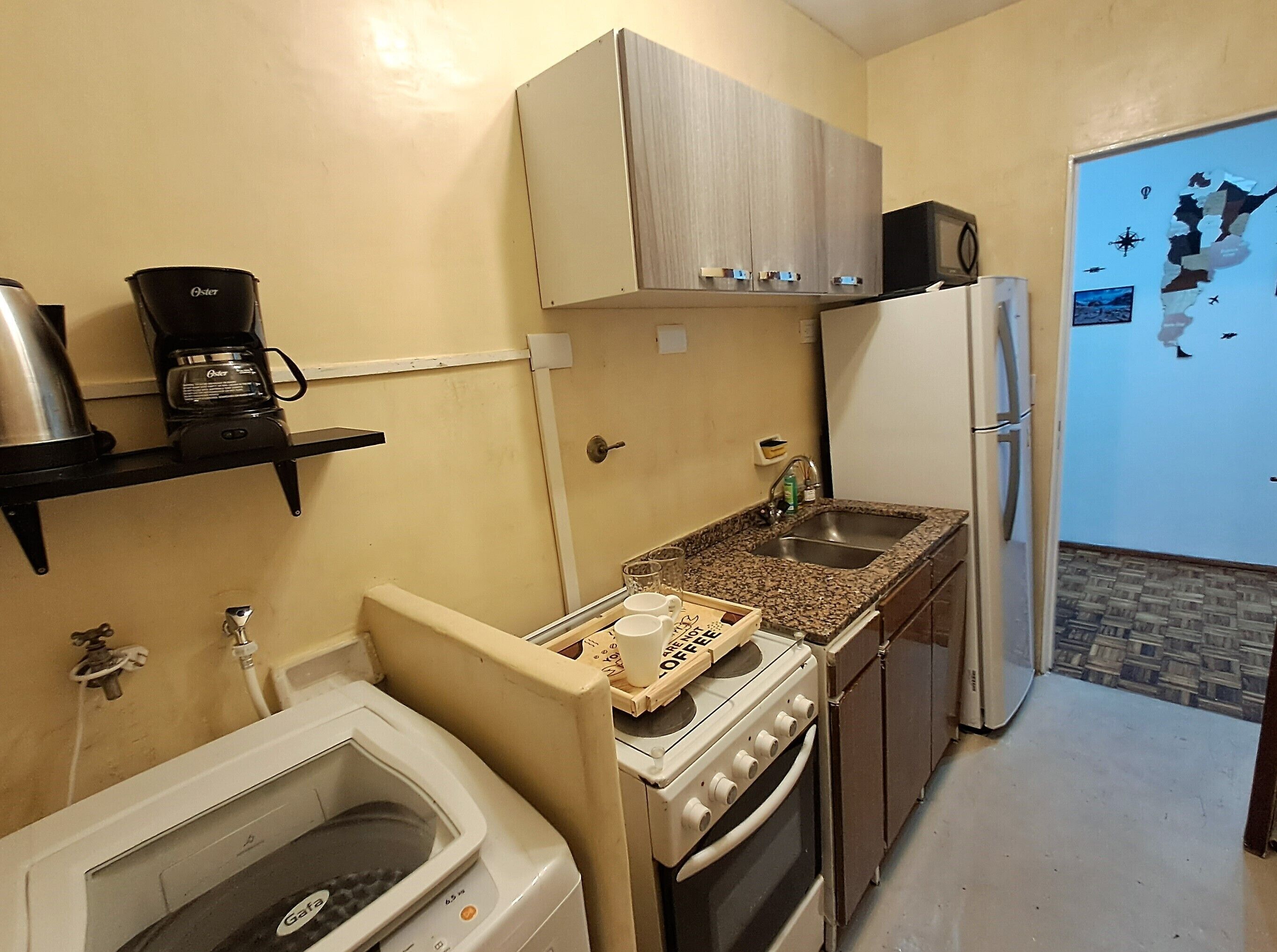 Una cocina compacta con horno integrado, refrigerador, cafetera y microondas.