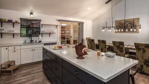 Une cuisine moderne dotée d’un grand îlot central, de meubles blancs et d’un coin repas avec des chaises à motifs.