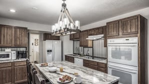 A modern kitchen with wooden cabinets, a marble countertop, a stainless steel refrigerator, and a built-in oven. - Bearadise - Upper Canyon Gem, Hot Tub, Game Room, HUGE deck (Ruidoso)