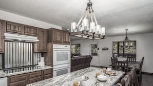 A modern kitchen with wooden cabinets, a marble countertop, and a dining area with a chandelier. - Bearadise - Upper Canyon Gem, Hot Tub, Game Room, HUGE deck (Ruidoso)