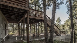 A rustic wooden structure with a staircase leading up to a platform, surrounded by tall trees. - Bearadise - Upper Canyon Gem, Hot Tub, Game Room, HUGE deck (Ruidoso)