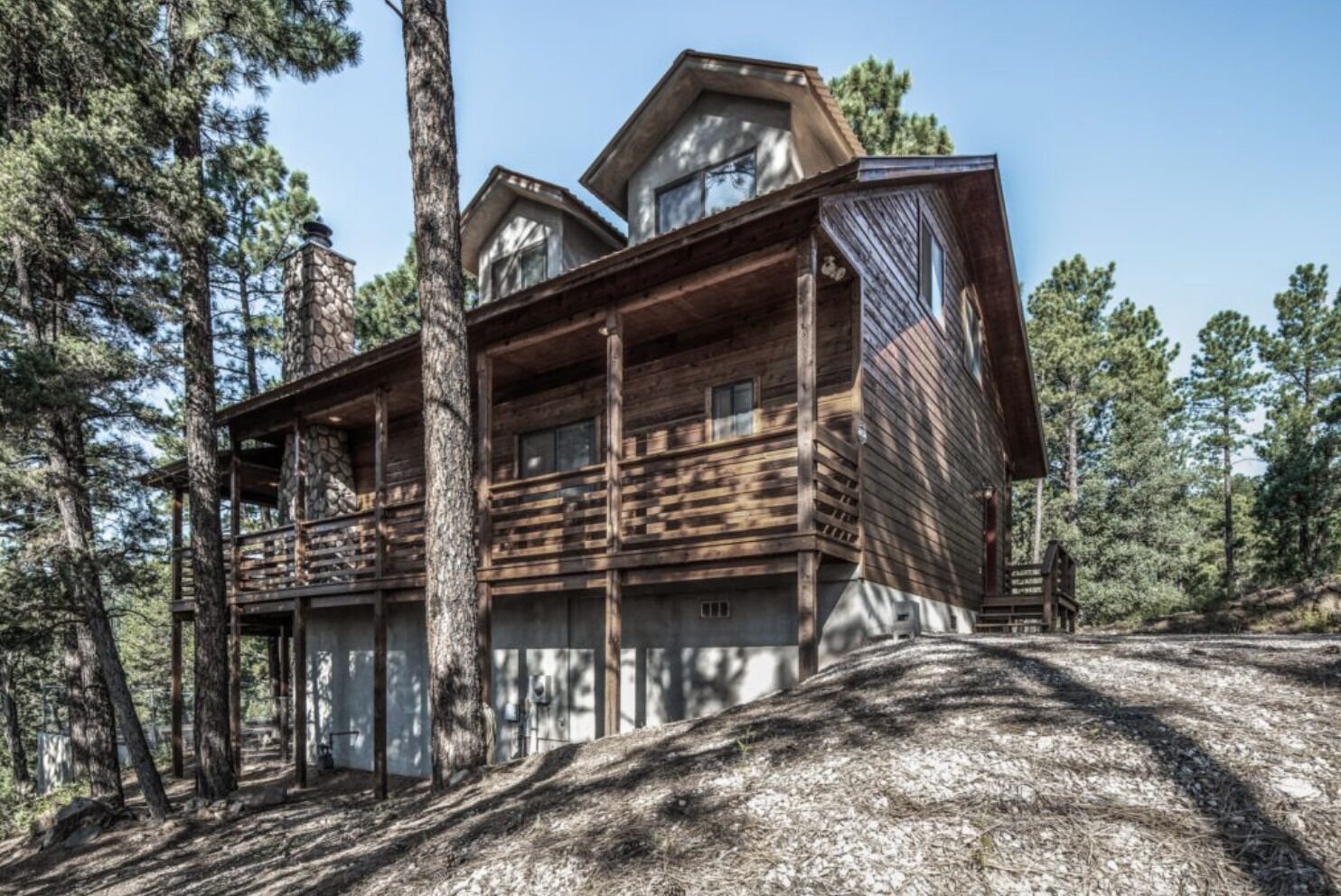 A log cabin with a balcony and a stone chimney, surrounded by trees.
