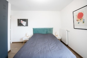 Una camera da letto con un letto, due comodini, un termosifone e due opere d'arte incorniciate alle pareti.