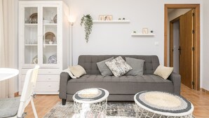 Un salon avec un canapé gris, deux petites tables d’appoint rondes, un meuble blanc et une porte en bois.