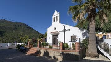 Una iglesia blanca con un campanario, rodeada por un muro de piedra y palmeras.