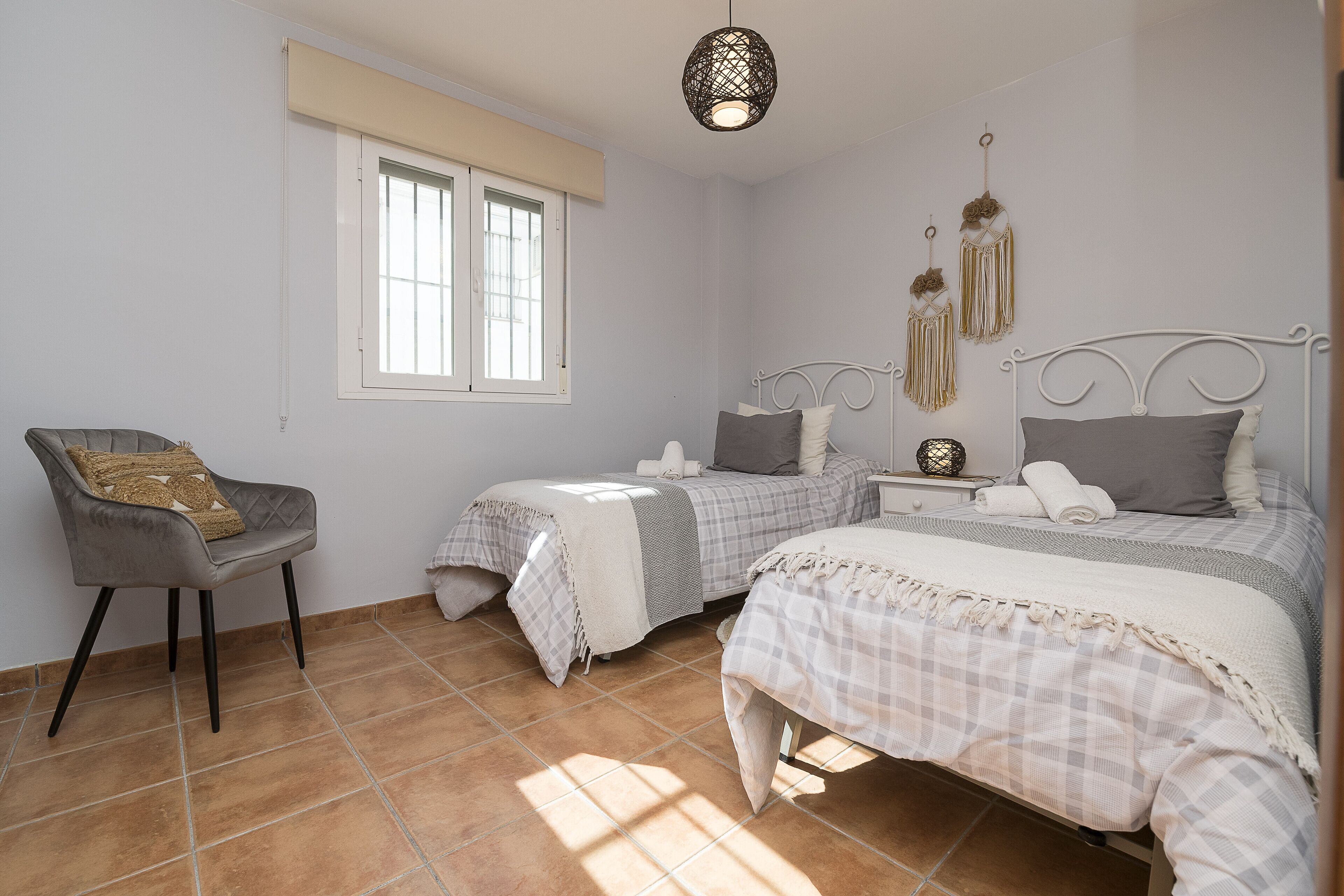 Een slaapkamer met twee bedden, een stoel, een raam en decoraties aan de muur.