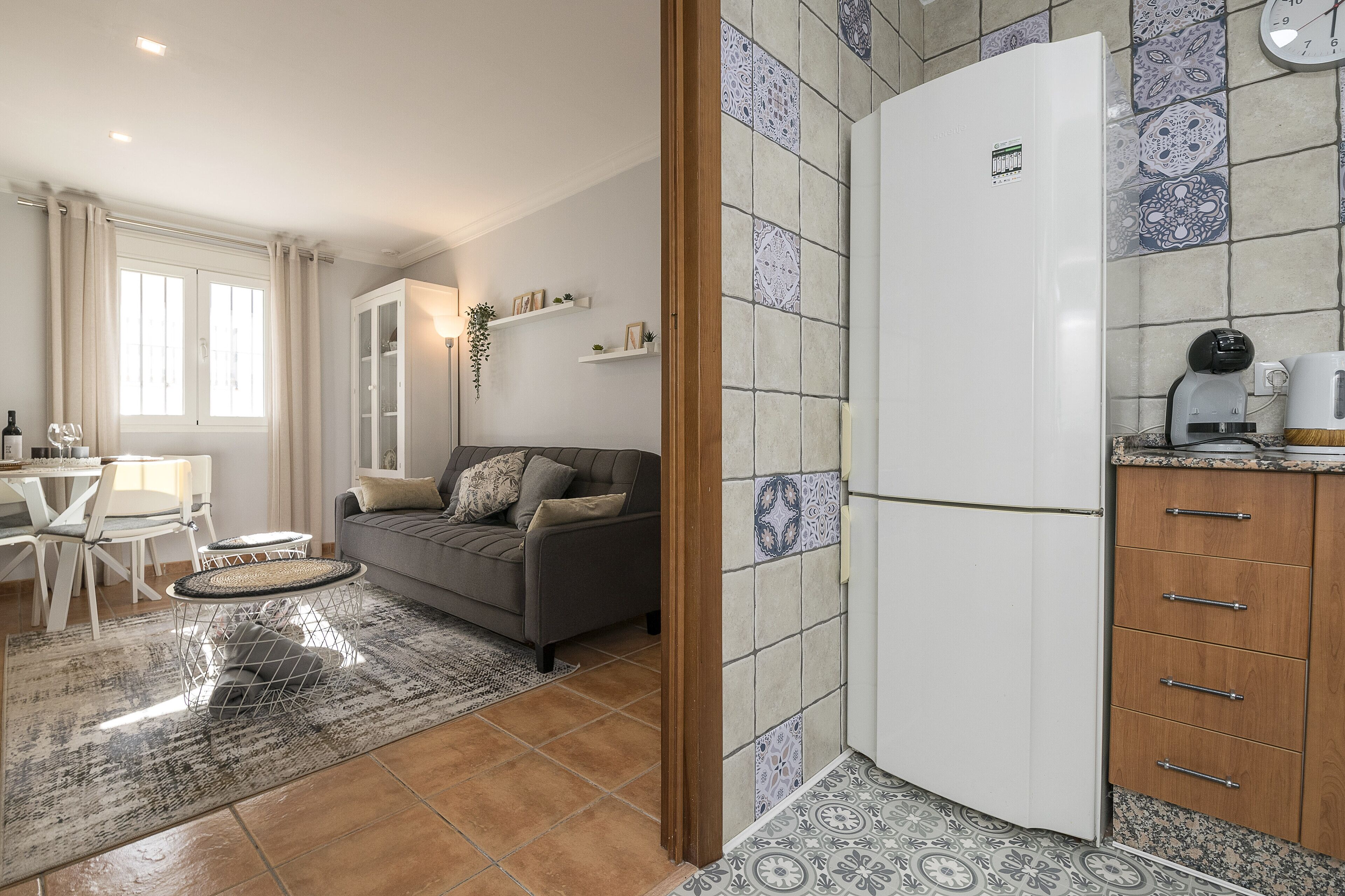 Een gezellige, compacte ruimte met een bank, een eethoek en een keuken met een koelkast en kastjes.