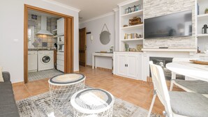 Un espace de vie compact comprenant une cuisine, un coin repas et un téléviseur fixé à un mur en pierre.