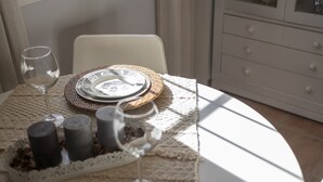 Une table dressée avec des assiettes, un verre et des bougies, avec une chaise et une commode en arrière-plan.