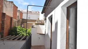 A narrow outdoor corridor with a white wall, a wooden door, and a window on the right. - Charming town house in the center of Roses, Costa Brava! Two rooms, 200 meters from the beach. Modern kitchen and balcony with sea views. (Roses)
