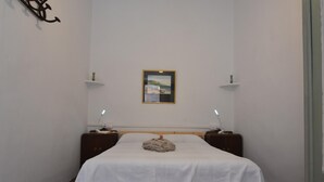 A small, neatly arranged bedroom with a single bed, two bedside tables, a wall-mounted shelf with a picture, and a small cabinet. - Charming town house in the center of Roses, Costa Brava! Two rooms, 200 meters from the beach. Modern kitchen and balcony with sea views. (Roses)