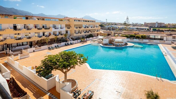 A hotel with a large pool, outdoor seating, and mountain views.