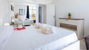 A hotel room with a large bed, a bedside table with a lamp, a wardrobe, and a view of the outdoors.