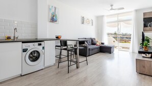 A modern kitchen with a built-in washing machine, a dining area with a table and chairs, and a grey sofa.