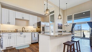A modern kitchen with white cabinets, a large island, and wooden flooring. - Spacious Luxury and Mountain Views (Colorado Springs)