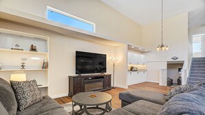 A modern living room with a flat-screen TV, grey sofas, a round coffee table, and a staircase leading to a kitchen. - Spacious Luxury and Mountain Views (Colorado Springs)