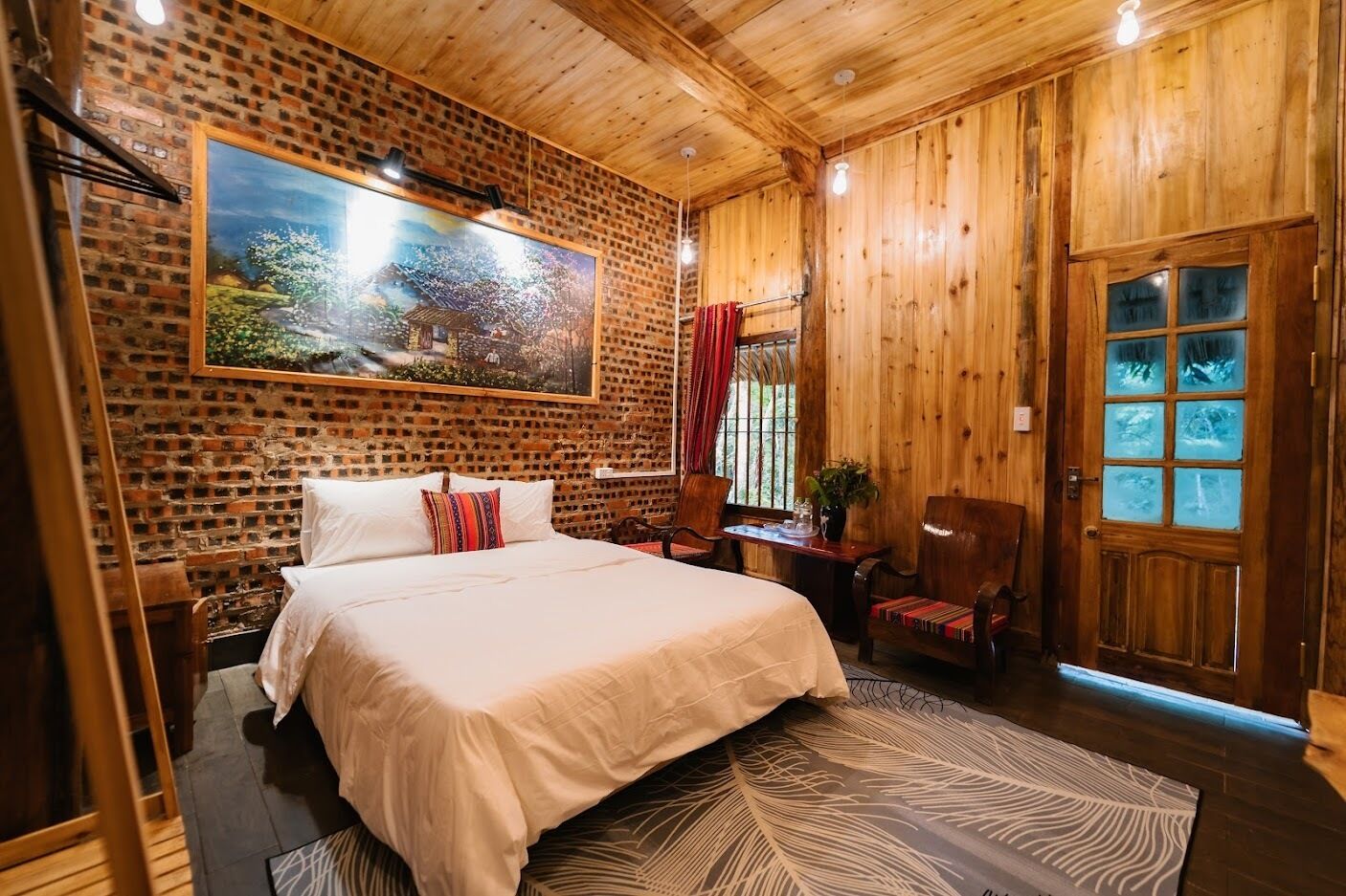 A wooden-paneled room with a large bed, a desk, and a door with frosted glass panels.