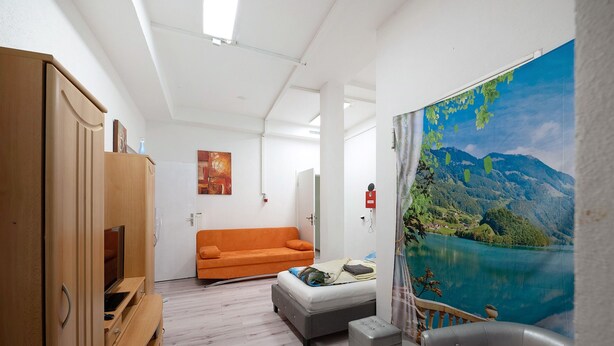 Une pièce comprenant un lit, un canapé, une armoire en bois et une grande fenêtre donnant sur la montagne.
