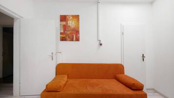 Ein Zimmer mit einer weißen Tür, einem Heizkörper und einem einzelnen orangefarbenen Sofa mit Kissen.