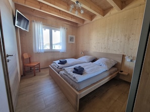 Ein Zimmer aus Holz mit einem Bett, einem Sessel, einem Fernseher und einem Fenster mit Vorhängen.