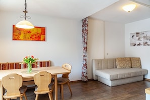 A dining area with a table, chairs, a vase of flowers, a sofa, and a wall with a floral curtain. - Holiday Apartment "Alpenflora 1" with Mountain View, Balcony & Wi-Fi (Ischgl)