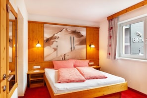 A wooden bed with red and white checkered bedding, a wall-mounted painting of a mountain, and two wall-mounted lamps. - Holiday Apartment "Alpenflora 1" with Mountain View, Balcony & Wi-Fi (Ischgl)