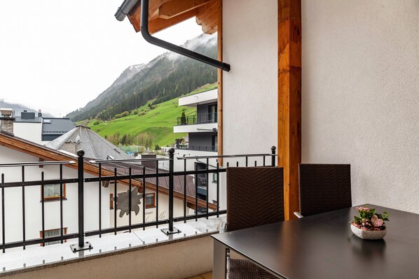 A balcony with a view of a mountain, a table with a flower vase, and a chair.