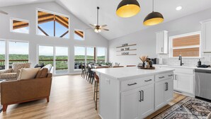 A spacious living area with a large island, a dining area with chairs, a sofa, and a view of the outdoors.