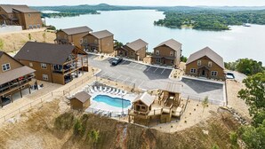 A resort with multiple wooden buildings, a swimming pool, and a view of a lake.