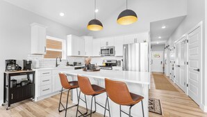 A modern kitchen with white cabinets, a central island with bar stools, a coffee machine, and a microwave.