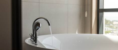 A modern bathroom with a large bathtub, a chrome faucet, and a window providing a view of the city.
