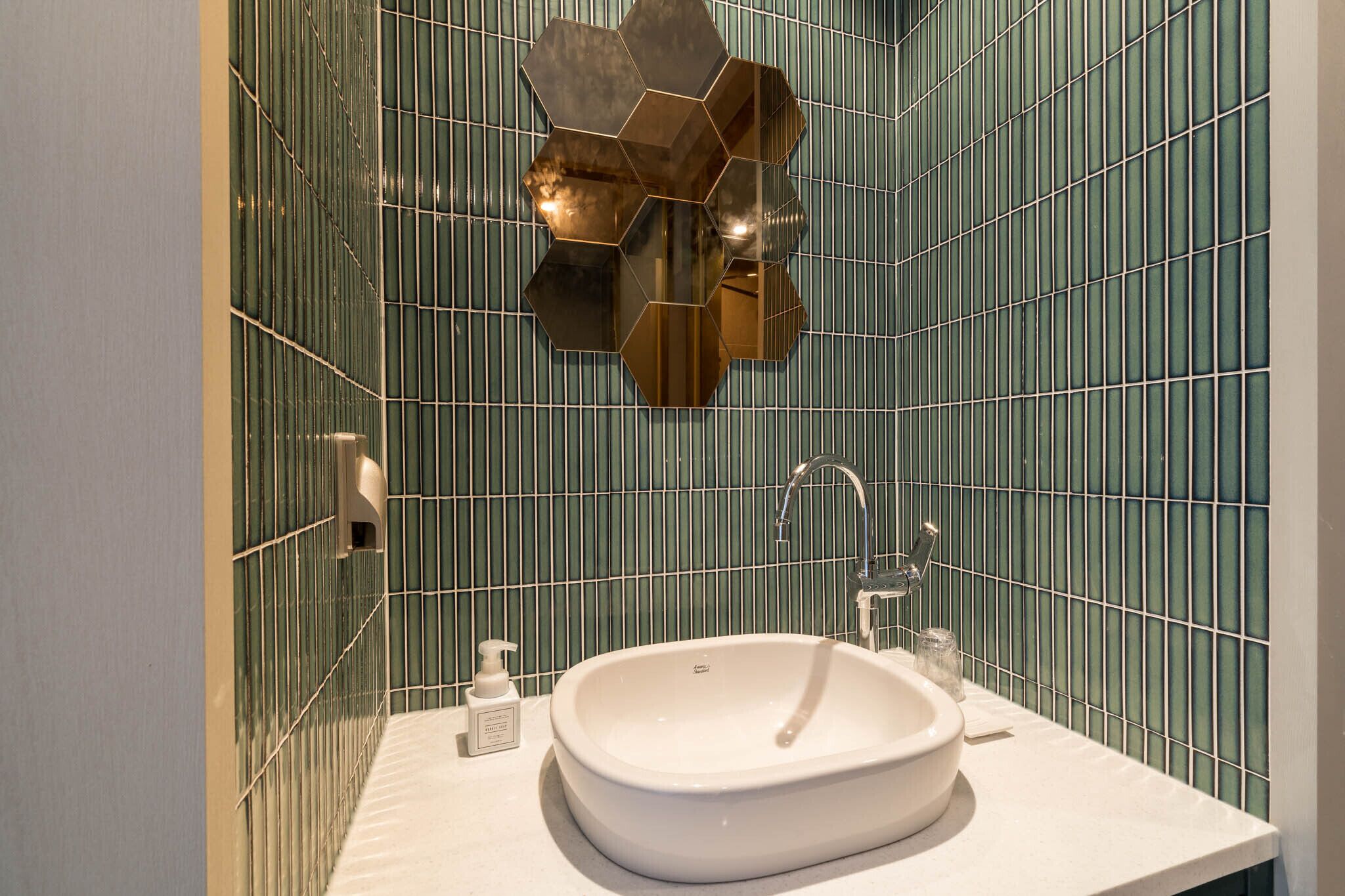 Un baño con un lavabo blanco, un espejo y una pared con azulejos verdes.