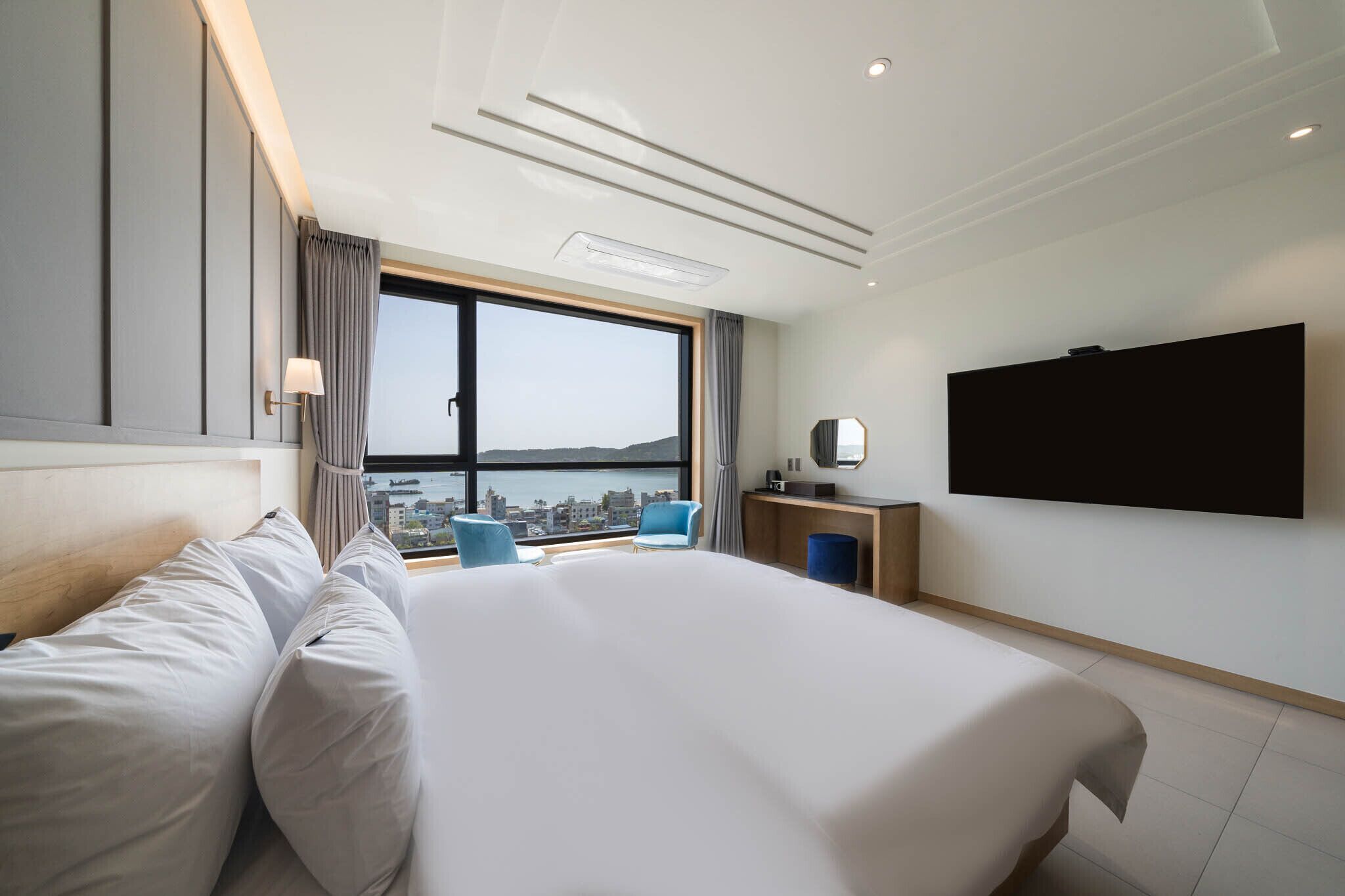 Une chambre d’hôtel moderne dotée d’un grand lit, d’un bureau, d’une télévision à écran plat et offrant une vue sur la ville grâce à une grande fenêtre.