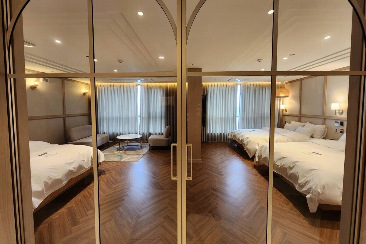 A hotel room with two beds, a sofa, a small table, and a large window with curtains.