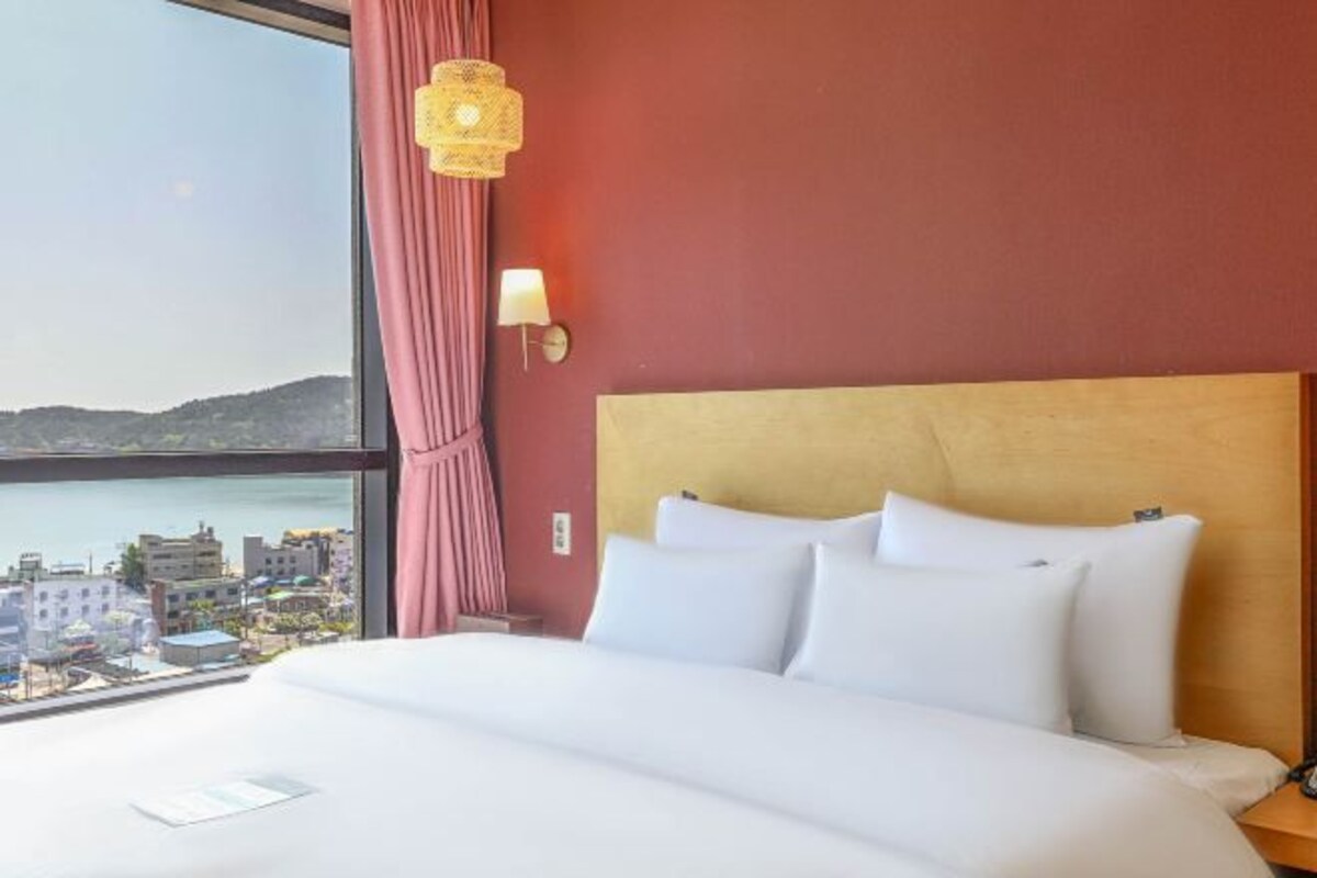 A hotel room with a large bed, a view of the city, and a window with curtains.