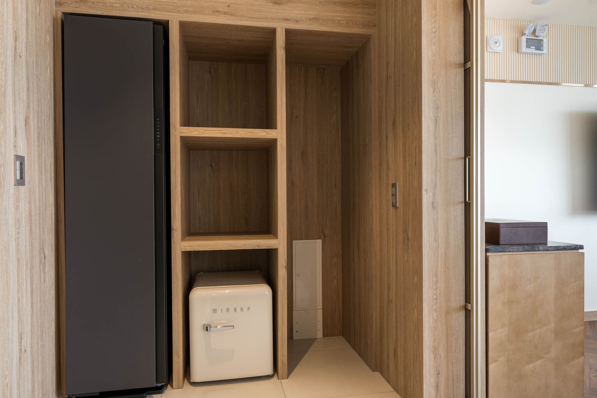 Una cocina compacta con armarios de madera, un refrigerador negro y un electrodoméstico blanco pequeño.