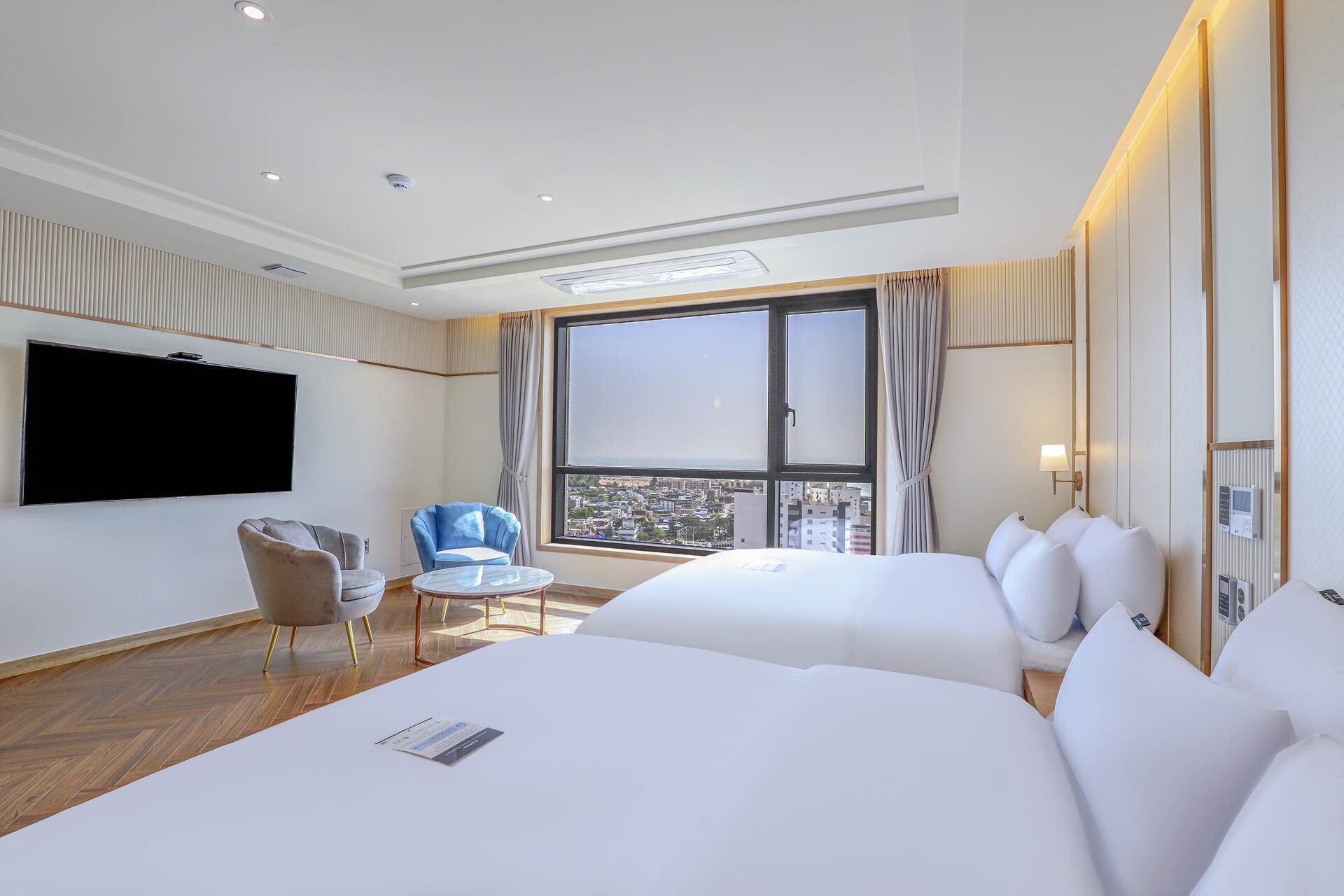 Une chambre d’hôtel avec deux lits, une télévision, une chaise et une vue sur la ville.