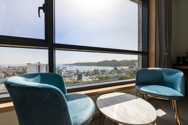 Habitación con dos sillas azules y una pequeña mesa redonda, ventanas amplias con vista a la ciudad y al agua.